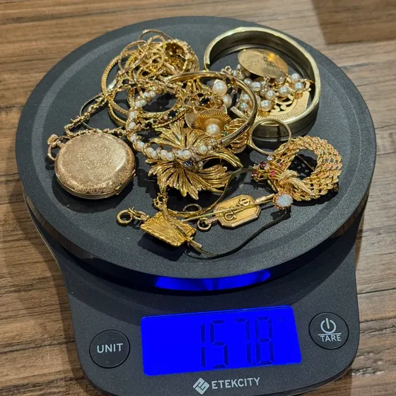 Gold jewelry from the $270 storage unit on a kitchen scale reading 157.8 grams: chains, bangles, a pocket watch, brooches and pearls