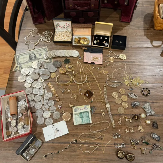 Everything spread on a table: jewelry box, pearls, gold chains, pocket watches, silver half dollars and dollars, silver certificates